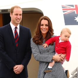 Kate Middleton, Prințul William și Prințul George coborară dintr-un avion. Kate e îmbrăcată într-o haină gri, Geroge e îmbrăcat în roșu, William e îmbrăcat în negru
